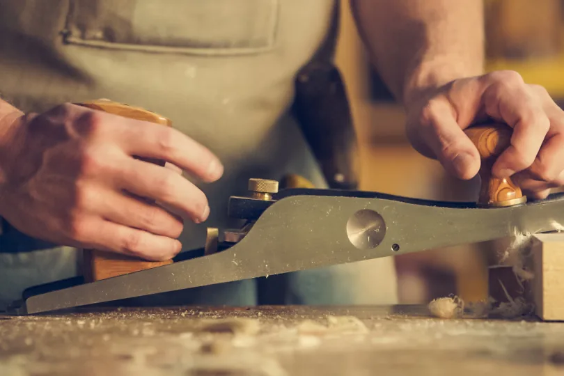 Operario trabajando una pieza de madera con un cepillo en su taller
